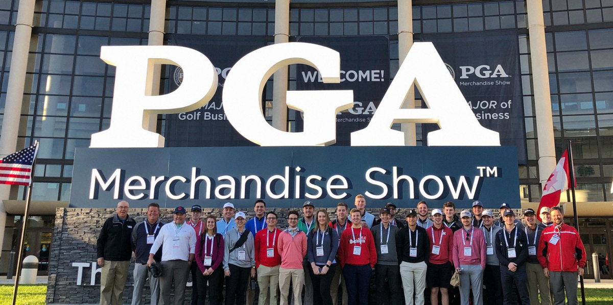 A group of PGA Merchandise Show attendees pose for a photo outside, in front of a large PGA sign.