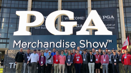 A group of PGA Merchandise Show attendees pose for a photo outside, in front of a large PGA sign.